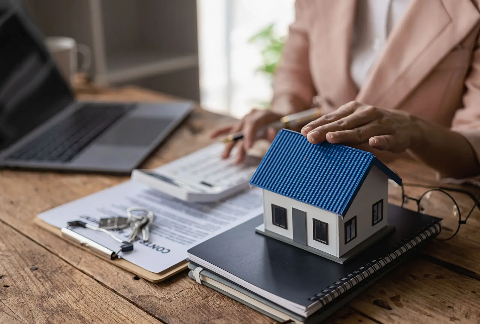 Person reviewing financial documents with a miniature house model on a tablet.